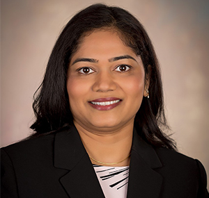 This is a portrait of a woman with dark hair, wearing a suit and smiling at the camera.