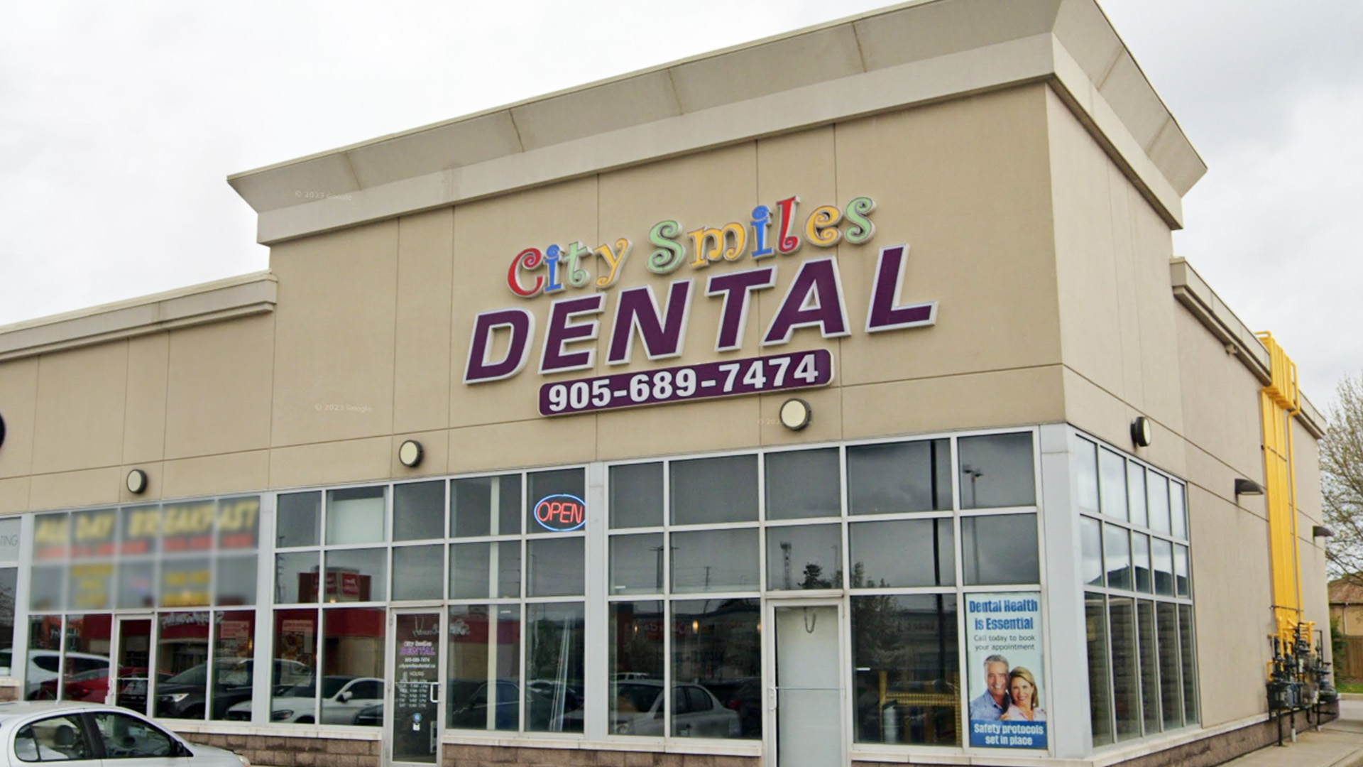 The image shows a dental clinic named City Smiles Dental with a sign indicating its name and contact information, featuring an exterior view of the building with a storefront window displaying promotional materials.